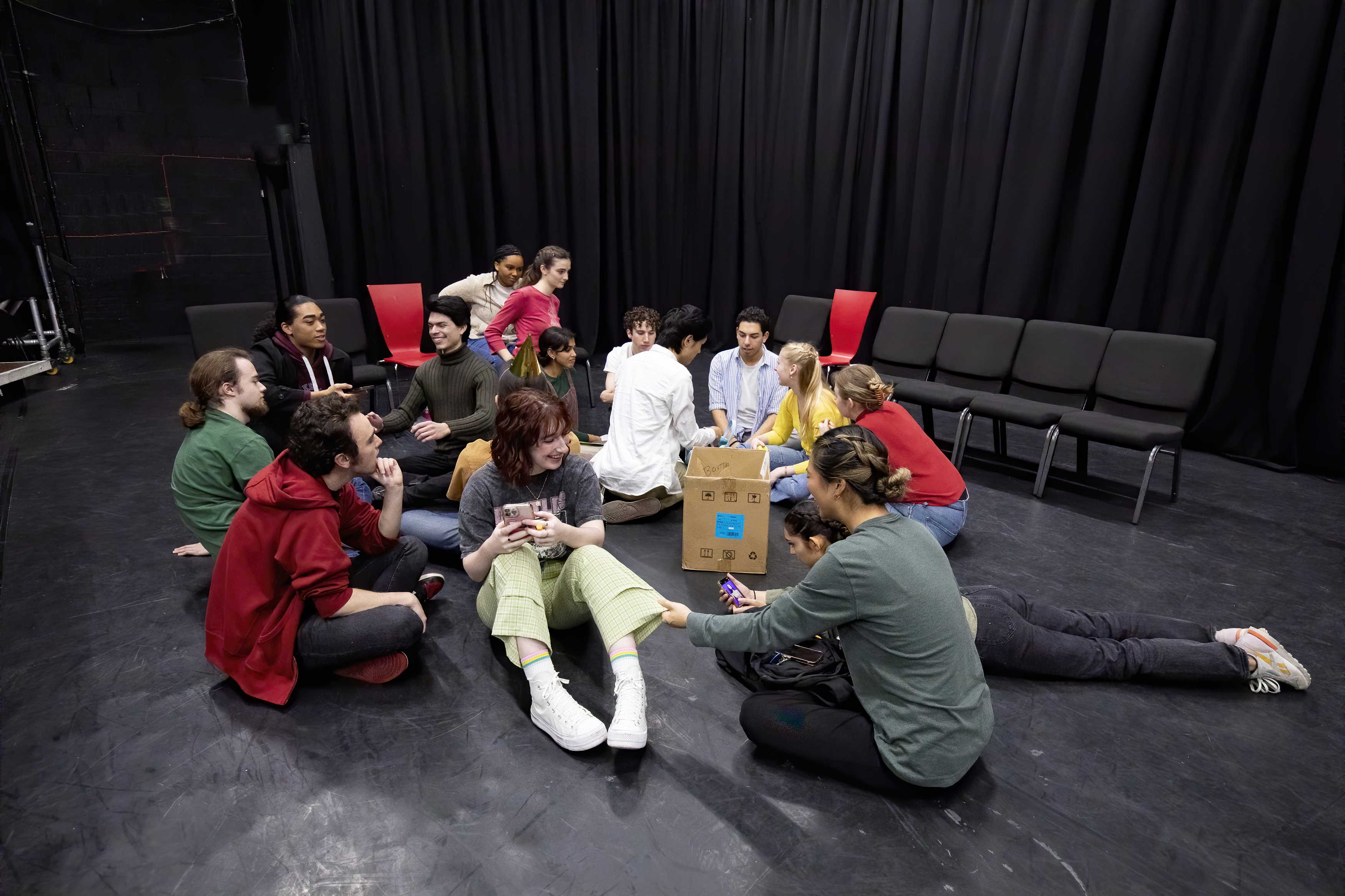 Fall 2022 students seated in a circle on the ground in a black box theatre